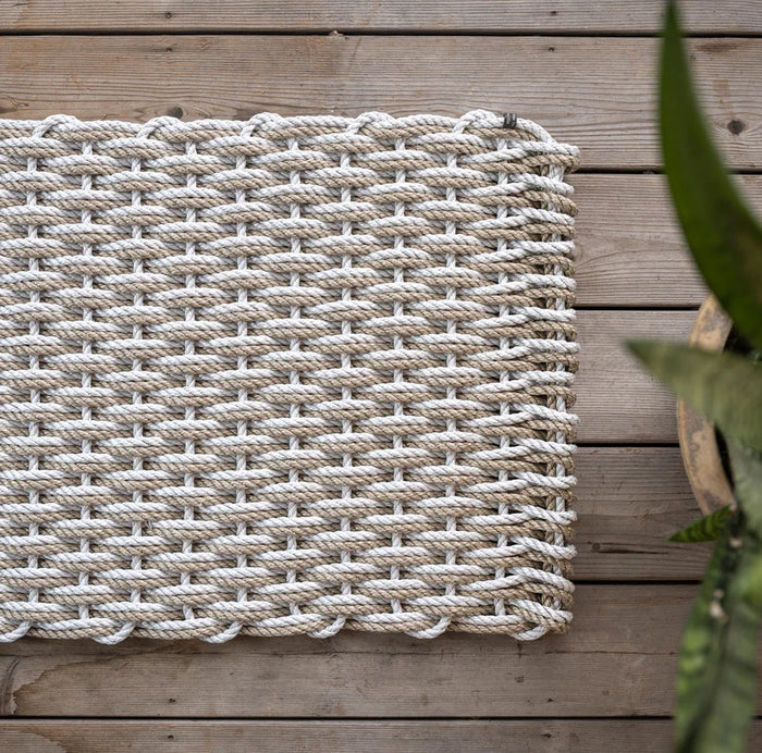 Handwoven Fog Grey and Sand Rope Doormat on a wooden deck, with a potted plant visible.