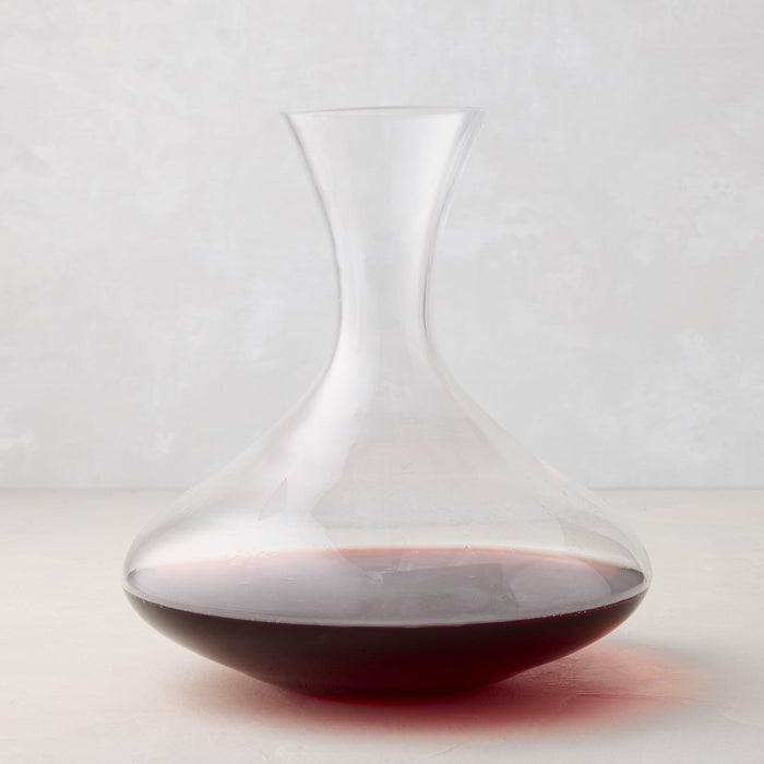 Clear mouthblown glass wine carafe with a broad base, curved neck, and red wine inside.