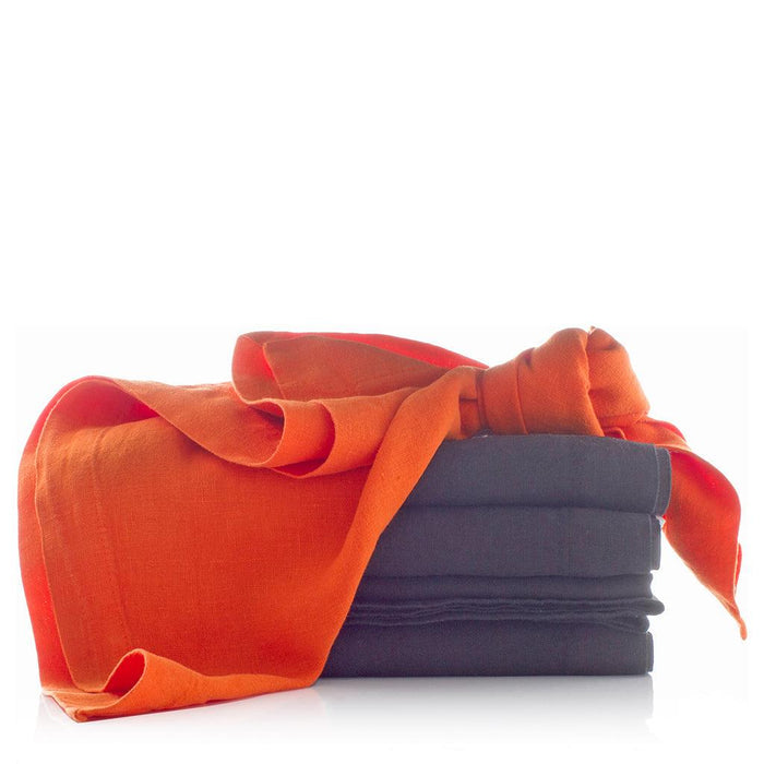 Stack of Graphite HG Signature hand-dyed linen napkins with an orange linen napkin tied around them.