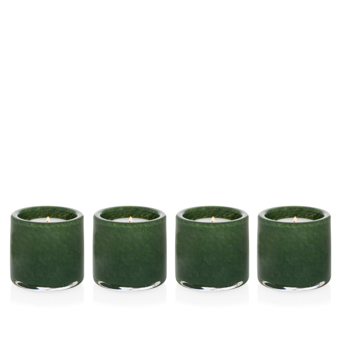 Four mouth-blown, hand-formed green votive glass candle holders with lit candles.