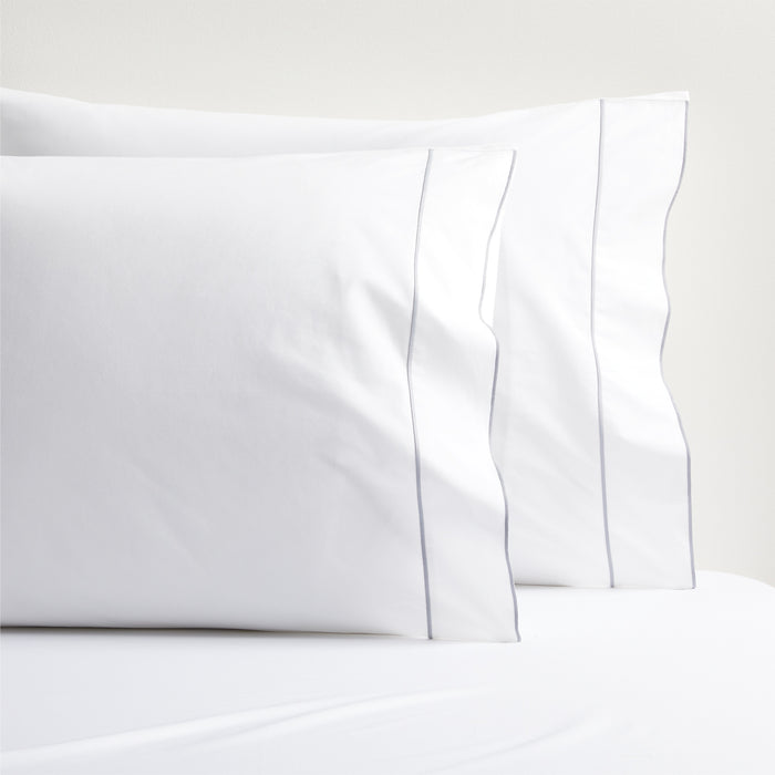 White percale pillowcases with a grey satin stitch border, stacked on a white sheet.