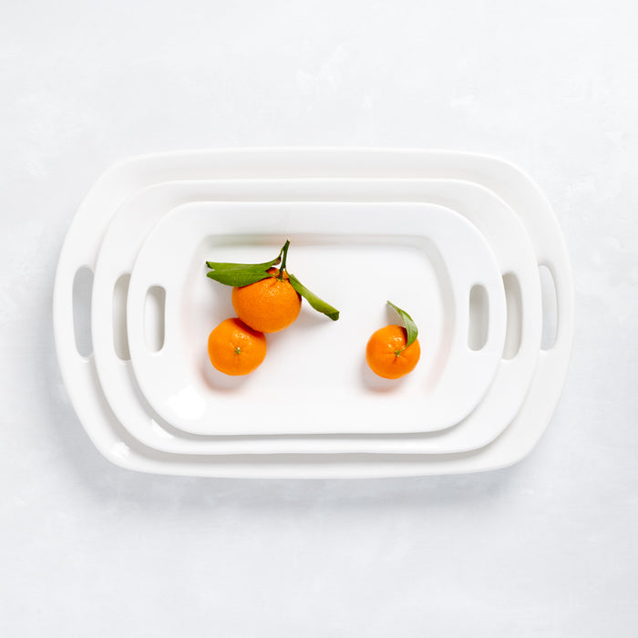 Set of 3 white ceramic serving platters with handles, nested, with tangerines.