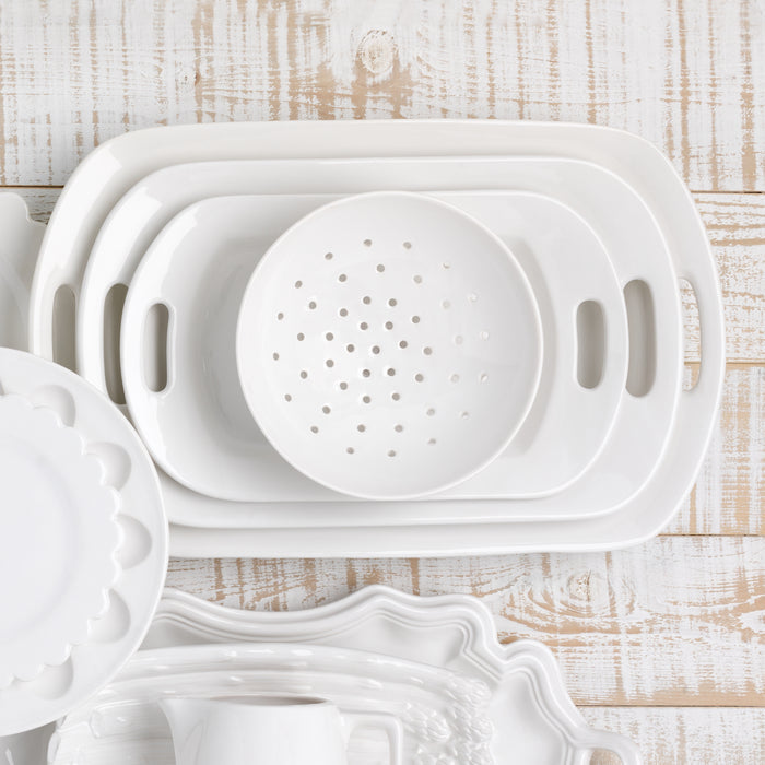 Set of 3 white ceramic serving platters with handles, nested on a distressed white wood surface.