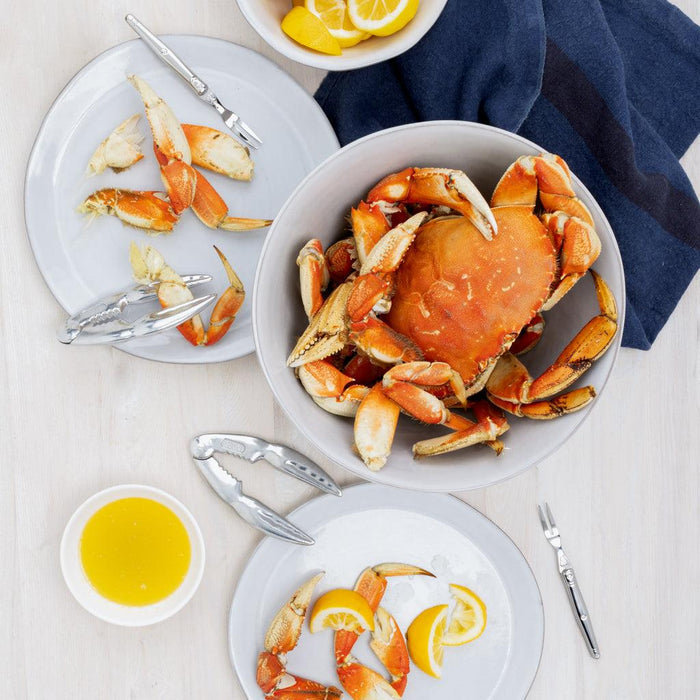 Overhead view of a large bowl of cooked crab, plates with crab legs, butter, and lemon slices.