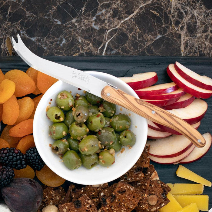 White ceramic dipping bowl filled with green olives, surrounded by fruit, crackers, and cheese.