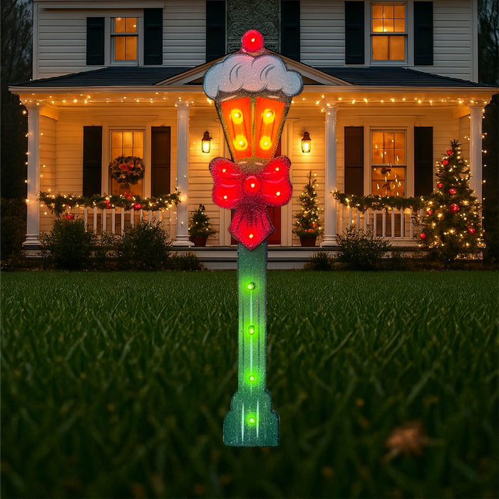 Christmas yard art featuring a lighted lamp post with candy canes and presents in red and green colors, displayed in a yard with a house and Christmas tree in the background.