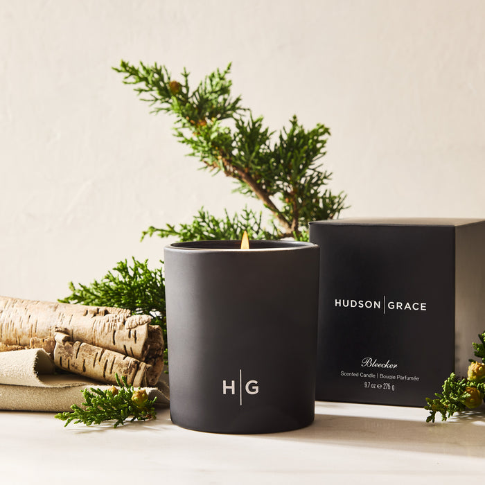 Hudson Grace Bleecker scented candle in a matte black glass vessel with a lit wick, next to its black box.