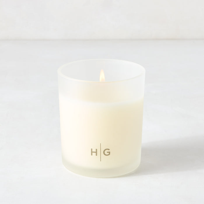 Hudson Grace Montecito Classic scented candle in a frosted glass vessel with "HG" logo, lit wick.