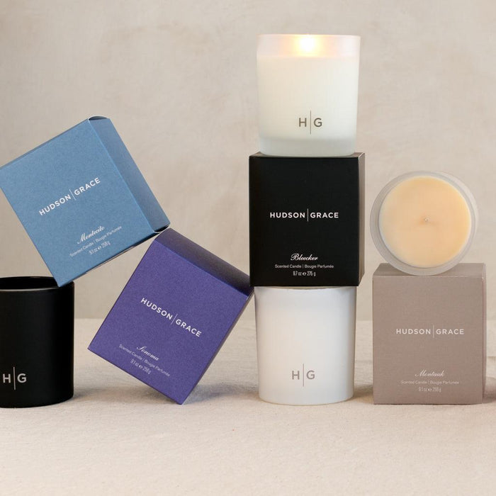 Hudson Grace scented candles in various colored glass vessels and gift boxes: white, black, blue, purple, and taupe.