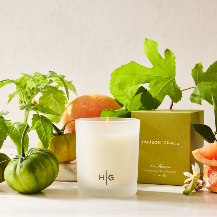 Hudson Grace San Marzano scented candle in a frosted glass vessel, lit, with green tomatoes, fig leaves, and grapefruit.