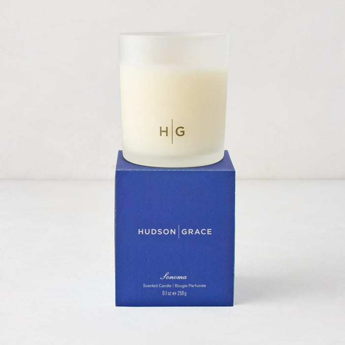Hudson Grace Sonoma Scented Candle in a frosted glass vessel with "HG" logo, on a blue gift box.