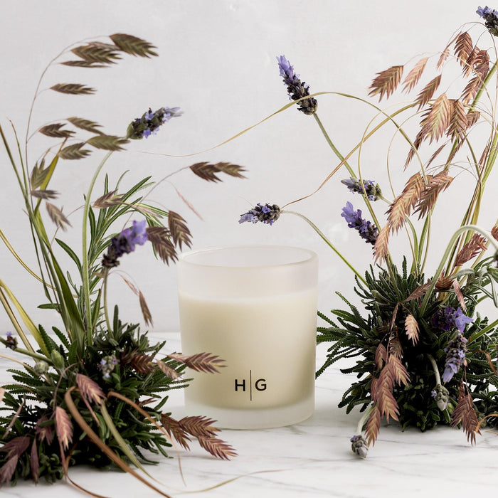Hudson Grace Sonoma Scented Candle in a frosted glass vessel with HG logo, surrounded by lavender and dried grasses.