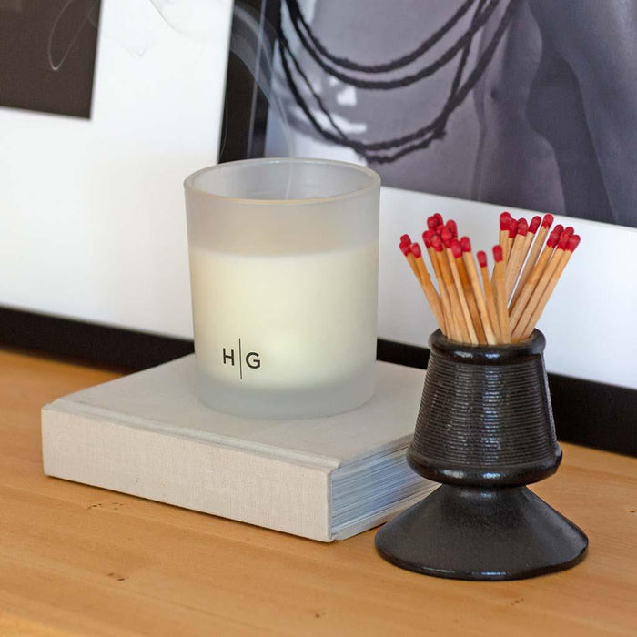 Hudson Grace Sonoma scented candle in a frosted glass vessel with "HG" logo, next to a black match holder with red-tipped matches.