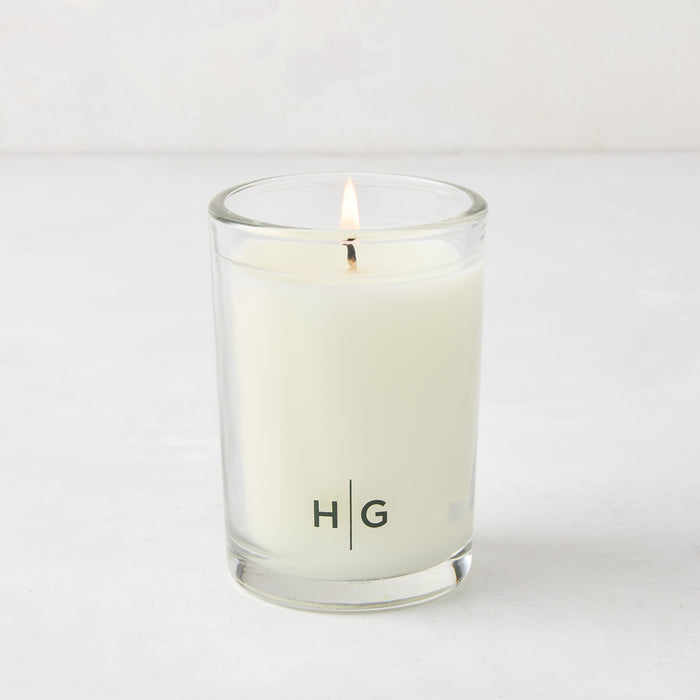 Hudson Grace Sweet Basil Kitchen Candle, white soy wax in clear glass votive with HG logo, lit wick.