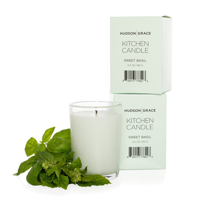 Hudson Grace Sweet Basil Kitchen Candle in a clear glass tumbler with two light green boxes and fresh basil.