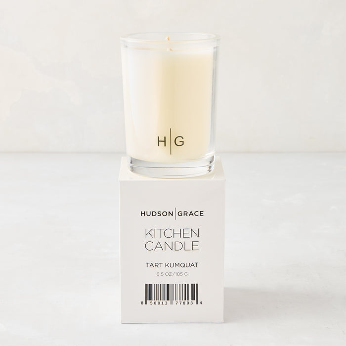Hudson Grace Tart Kumquat Kitchen Candle in a clear glass votive with HG logo, on its white box.