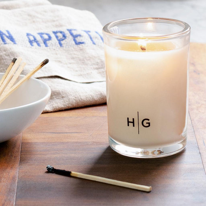 Hudson Grace Tart Kumquat Kitchen Candle, white soy wax in a clear glass jar with "HG" logo, lit wick.
