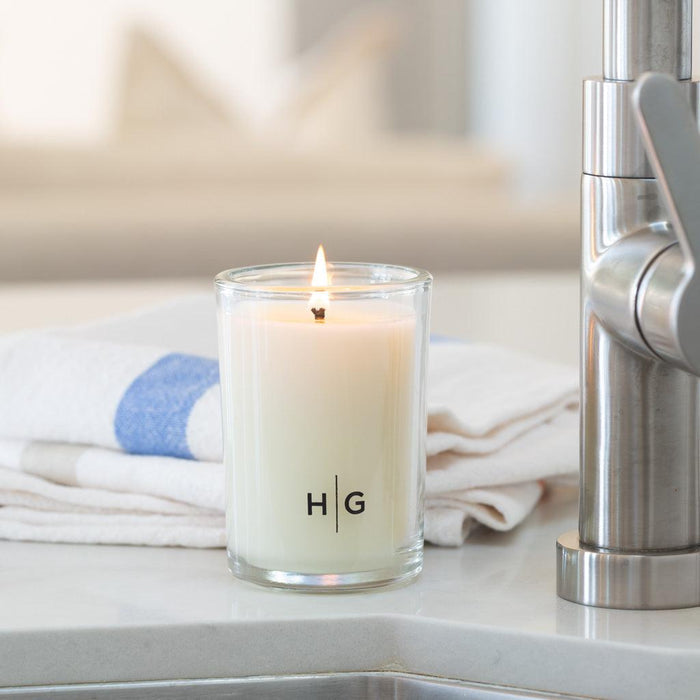 Hudson Grace Tart Kumquat Kitchen Candle, white soy wax in clear glass jar with "HG" logo, lit wick.