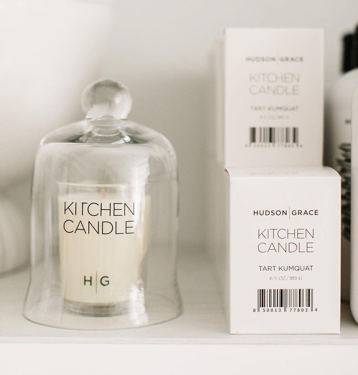 Hudson Grace Tart Kumquat Kitchen Candle in a clear glass cloche, with two white product boxes.