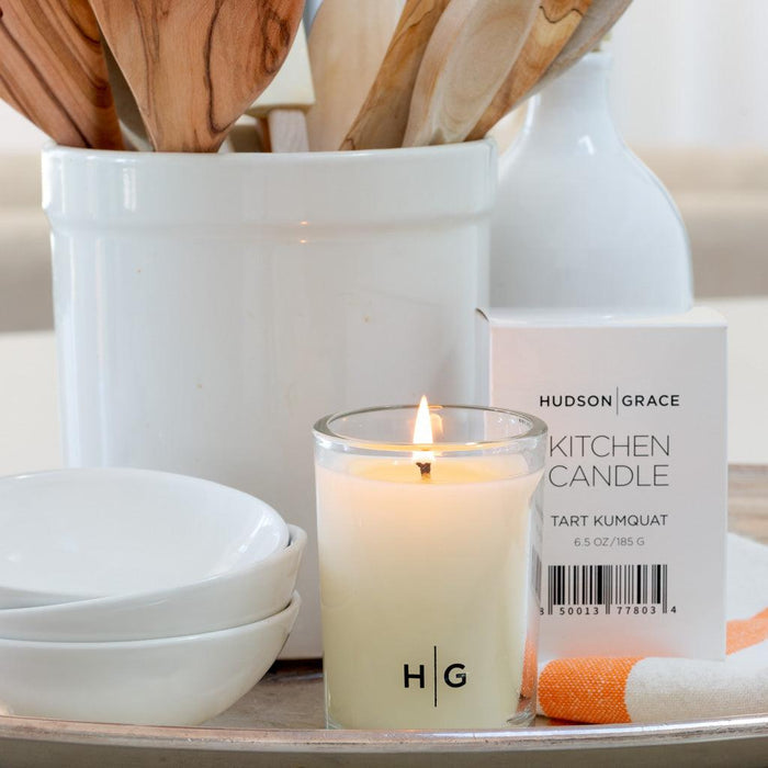 Hudson Grace Tart Kumquat Kitchen Candle in a clear glass jar with "HG" logo, next to its white box.
