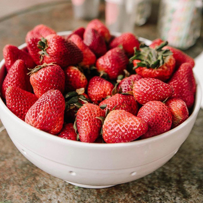 White ceramic colander filled with fresh red strawberries.