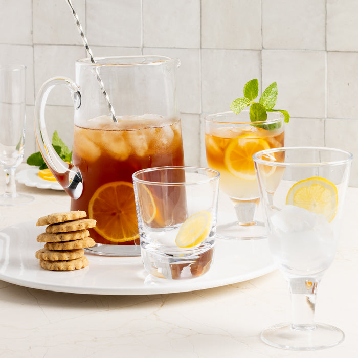 Clear Hudson Stemless Glass with a lemon slice, alongside a pitcher and other glasses with iced tea and cookies.