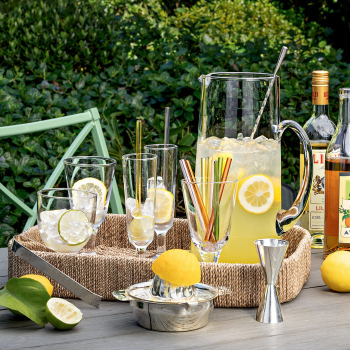 Clear Hudson Water Goblet, chunky glass style, on a woven tray with lemonade and citrus.