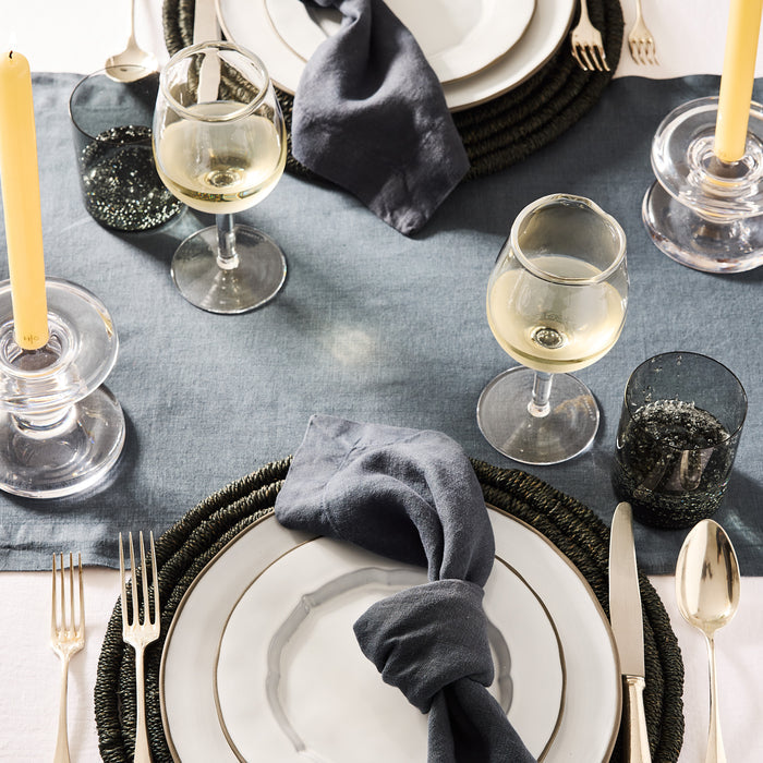 Indigo HG Signature hand-dyed linen napkin, 22-inch square, knotted on a white plate at a set table.