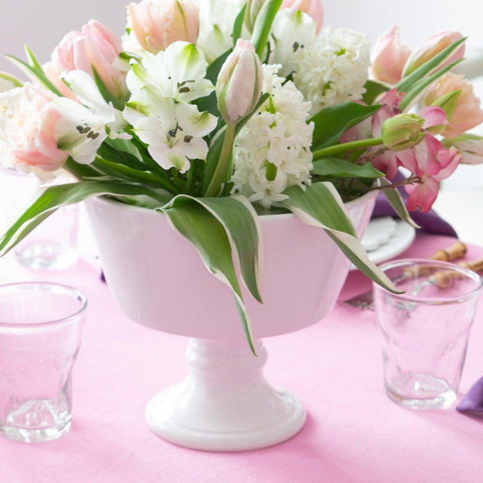 White Italian ceramic compote bowl with a footed base, holding a bouquet of pink and white flowers.