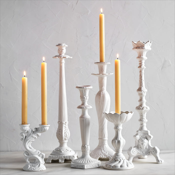 Collection of ornate white Italian ceramic candlesticks with intricate detailing and lit taper candles.