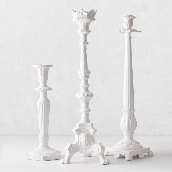 Three white Italian ceramic candlesticks with intricate antique-style detailing on a light background.