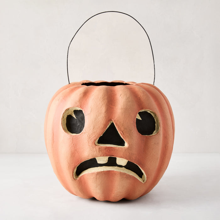 Handcrafted, distressed orange papier-mâché Jack O' Lantern candy bucket with a sad face and black wire handle.