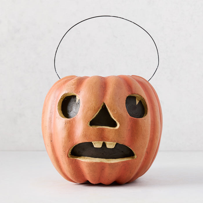 Distressed orange papier-mâché Jack O' Lantern candy bucket with a surprised face and wire handle.