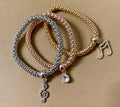 Three bracelets laid out on a surface, featuring gold, silver, and rose gold colors with rhinestone musical charms on each.