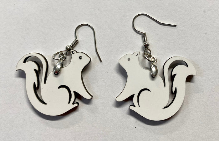 A pair of laser cut wooden earrings in the shape of white squirrels with hollow tail designs.