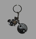 Keychain with yin yang design and small figures on a gray background
