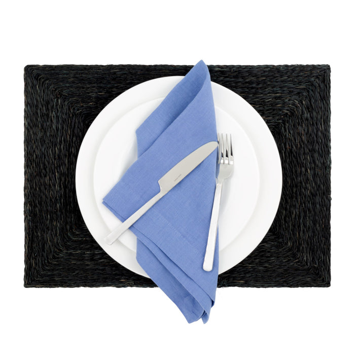 Black abaca woven rectangular placemat with white plates, blue napkin, and silverware.