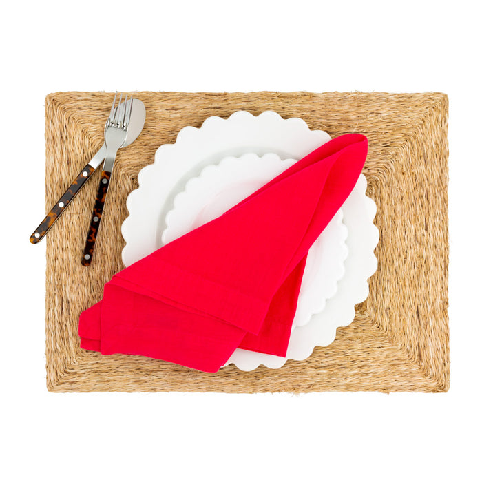 Natural abaca woven rectangular placemat with white scalloped plates, red napkin, and tortoise-handle flatware.
