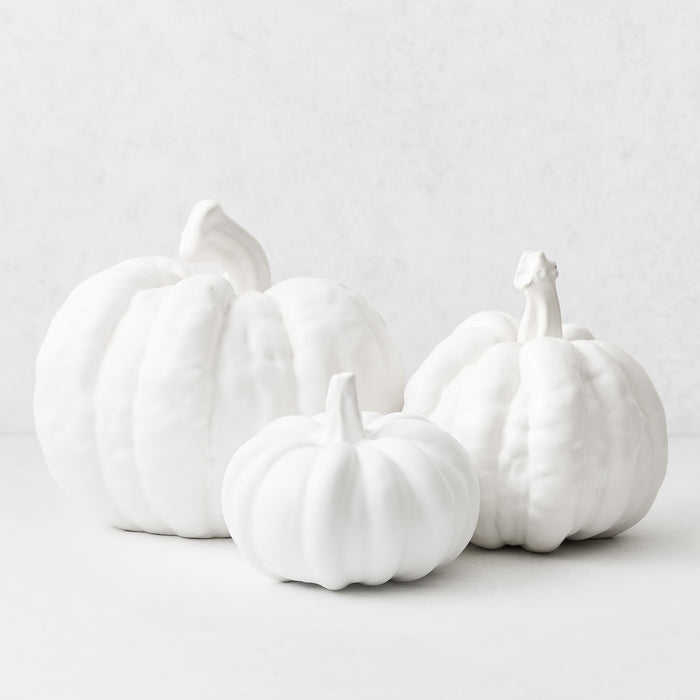 Three matte white ceramic pumpkins of varying sizes on a white background.