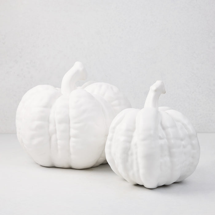 Two matte white ceramic pumpkins, one large and one small, with ribbed texture.