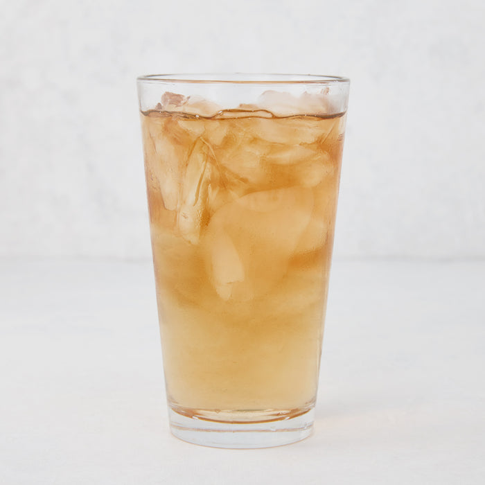 Tall, clear Hudson Grace glass filled with ice and a brown beverage.