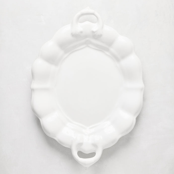 White oval ceramic serving platter with scalloped edges and handles.