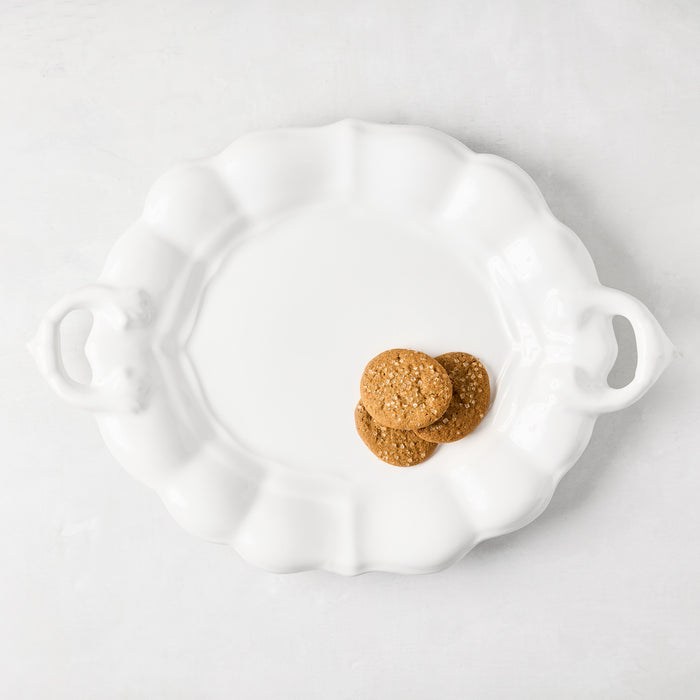 White ceramic oval serving platter with scalloped edges, handles, and three cookies.