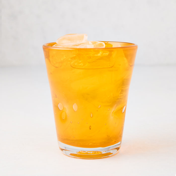 Light orange Henri mouth-blown glass, 8 oz, with ice, showing unique imperfections and air bubbles.
