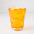 Light orange Henri mouth-blown glass, 8 oz, with ice, showing unique imperfections and air bubbles.