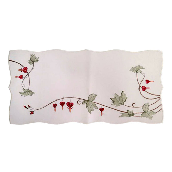White embroidered linen table runner featuring traditional bleeding heart flowers, green vine accents, and scalloped edges in a German-inspired floral design.