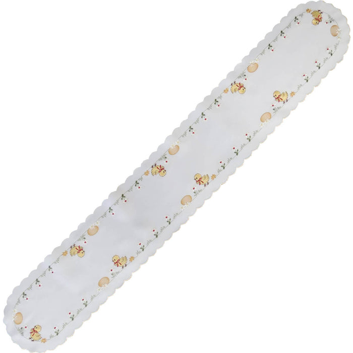 White satin table runner with scalloped edges, embroidered with yellow chicks, Easter eggs, and spring daisies.