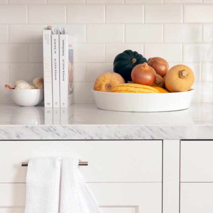 White ceramic Luce Large Serving Dish filled with gourds and onions on a marble counter.