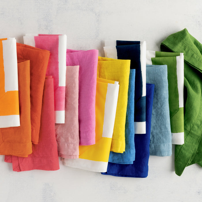 Row of hand-dyed linen napkins in various vibrant colors like orange, pink, yellow, blue, and green.