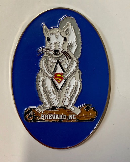 An oval metal magnet featuring a white squirrel wearing a Superman costume, with a blue background and the text 'BREVARD, NC' at the bottom.